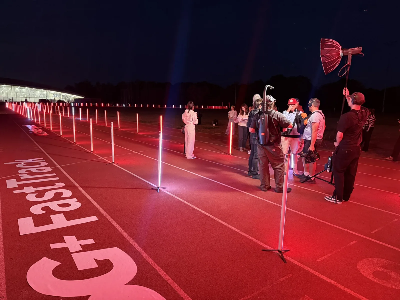 A film crew filming an illuminated running track installation at night, lined with glowing red markers
